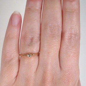 May include: A simple gold band ring with a small, clear gemstone set in the center.