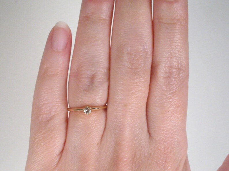 May include: A simple gold band ring with a small, clear gemstone set in the center.