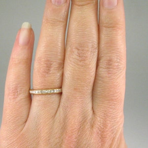 May include: A gold band ring with a row of small, clear diamonds set in a channel setting.