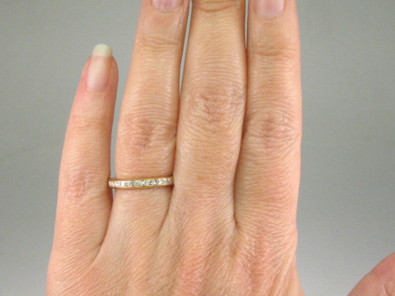 May include: A gold band ring with a row of small, clear diamonds set in a channel setting.