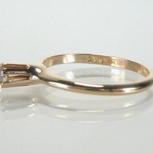 May include: A simple gold band ring with a single, small, round diamond set in a prong setting. The ring is marked "9KT" on the inside of the band.