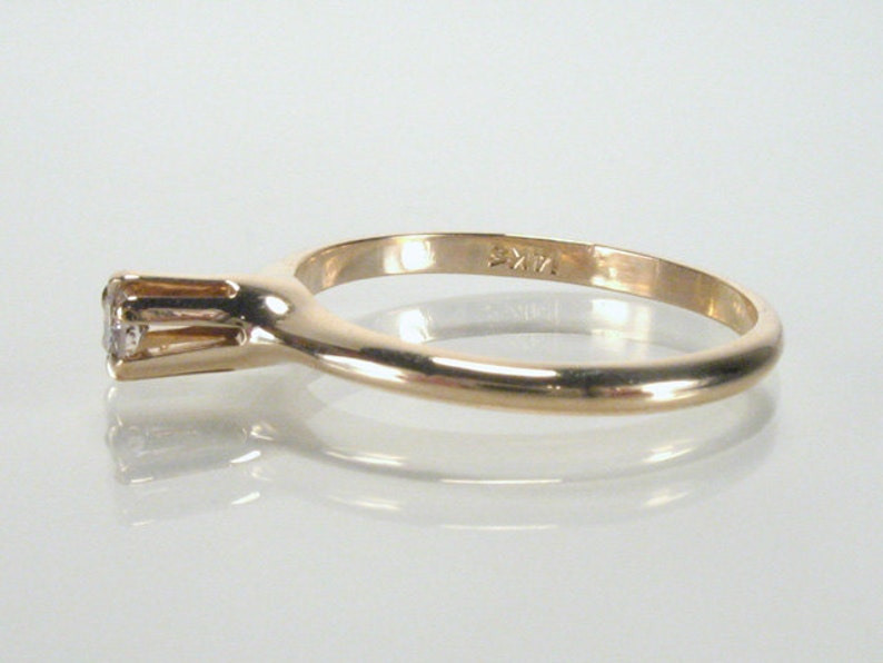 May include: A simple gold band ring with a single, small, round diamond set in a prong setting. The ring is marked "9KT" on the inside of the band.