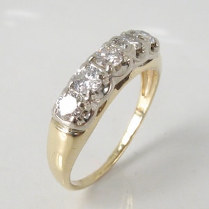 Puede incluir: Un anillo de banda de oro con una fila de cinco diamantes transparentes engastados en un engaste de metal blanco.