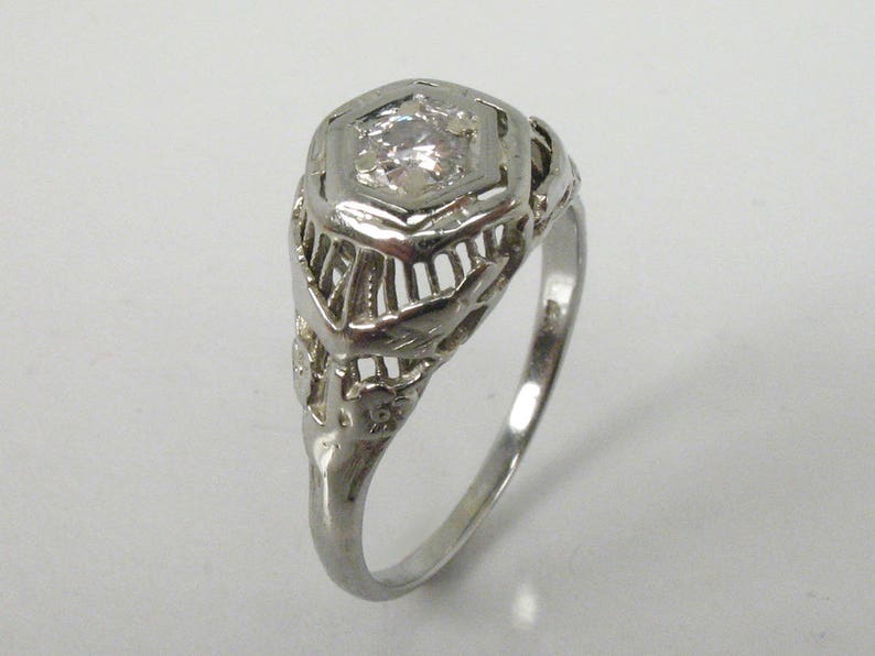 May include: A silver ring with a delicate filigree design and a single round clear stone in the center.