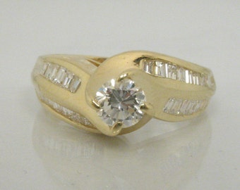 May include: A gold ring with a large round diamond in the center and smaller baguette diamonds set in the band.