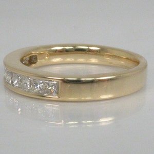 May include: A gold band with a row of small square-shaped diamonds.