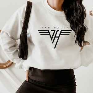 May include: White sweatshirt featuring the band name "Van Halen" in black block letters above a black and white logo. The logo consists of a stylized "VH" with horizontal lines above. The sweatshirt is a casual, comfortable style.