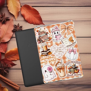 Puede incluir: Un lector electrónico negro con una funda transparente con pegatinas con temática otoñal. Las pegatinas incluyen calabazas, libros, fantasmas y tazas de café sobre un fondo a cuadros naranja y blanco. El texto incluye "pumpkin spice girlie" y "Cozy Readers Book Society".