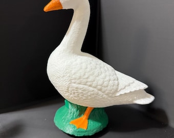 May include: White plastic goose figurine with orange beak and feet, standing on a green base.