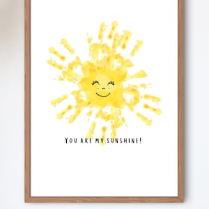 May include: A framed print with a yellow sun made from handprints. The sun has a smiling face and the text "You are my sunshine!" is printed below.