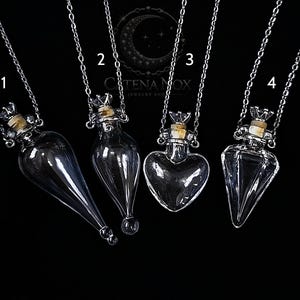 May include: Four glass vial necklaces with silver chains, each with a unique shape: a teardrop, a bulbous shape, a heart, and a faceted design. Each vial has a cork stopper and a decorative silver crown-like cap. The background is black.