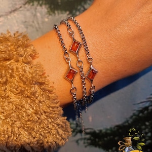 May include: Three silver chain bracelets with amber-coloured rectangular stones. The bracelets are layered on a person's wrist. The image has the text "Nature Spirits" at the bottom.