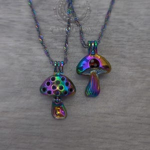 Könnte beinhalten: Zwei Halsketten mit schillernden Pilzanhängern. Die Pilzanhänger haben ein Regenbogen-Finish und sind an passenden gedrehten Seilketten befestigt. Die Pilzkappen haben eine Reihe kleiner Löcher. Der Hintergrund ist ein hellgraues Holzmaserung.