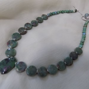 May include: A green and pink gemstone necklace with a large pendant. The necklace is made of round beads and has a silver clasp.