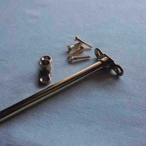 May include: A selection of brass hardware components, including a long rod, a small bracket, and several screws. The items are arranged on a light blue surface, suggesting a set for furniture or a similar project.