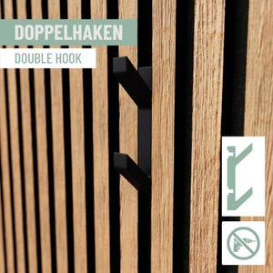 Könnte beinhalten: Ein schwarzer Doppel-Haken an einer Holzlattenwand. Die Wand besteht aus vertikalen Holzlatten mit natürlicher Holzmaserung. Der Text "DOUBLE HOOK" ist im Bild zu sehen.