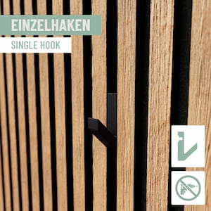 Könnte beinhalten: Ein schwarzer Einzelhaken an einer Wand aus Holzlatten. Die Wand hat vertikale Holzlatten mit schwarzen Zwischenräumen. Der Text "EINZELHAKEN" ist sichtbar.