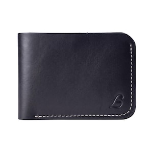 May include: A dark navy blue bifold wallet featuring a smooth finish and contrasting white stitching along the edges. The bottom right corner displays a small, embossed letter B logo, and the right side has a rounded corner design.