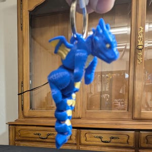 Blue Babby Scruff Dragon Articulated Keychain. Uroczy, noszony jak kociak przez mamę. Sprawdź całą naszą linię Littles.