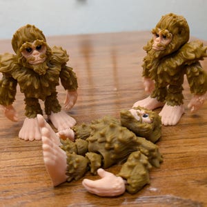 May include: Three brown furry figures with pink feet. Two are standing upright and one is lying on its back with its legs in the air.