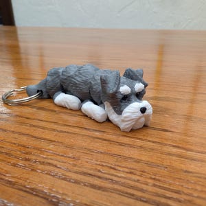 May include: A grey and white miniature schnauzer keyring. The keyring is made of plastic and has a silver metal ring.