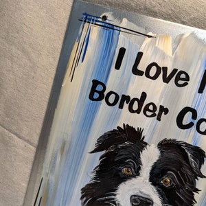 Puede incluir: Un letrero pintado con un perro Border Collie con pelaje blanco y negro y ojos marrones. El letrero tiene las palabras "I Love Border Collies" en letras negras sobre un fondo azul y blanco.