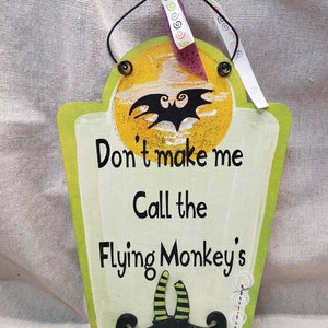 May include: A green wooden sign with a yellow moon and a black bat silhouette. The sign reads "Don't make me call the Flying Monkey's".  The sign has a black and green witch's shoe with purple polka dots at the bottom.