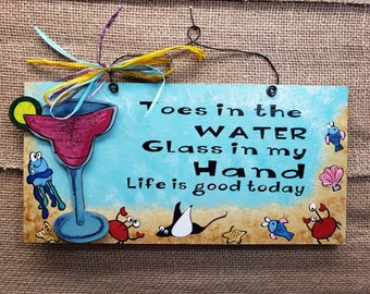 Letrero de madera pintado a mano con margaritas y dedos de los pies en el agua para la playa.