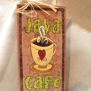 May include: A wooden sign with a brown background and a green and white design. The sign says "Java Cafe" and features a cartoon coffee cup with a heart and steam.