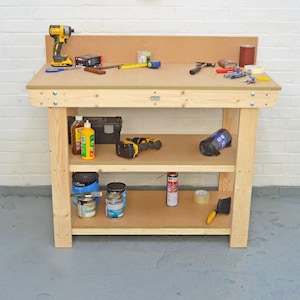 May include: A wooden workbench with two shelves. The workbench has a light wood finish and is made of solid wood. The workbench is 183 cm long and 61 cm wide. The workbench has a backsplash and a tool tray. The workbench is ideal for a garage, workshop, or basement.