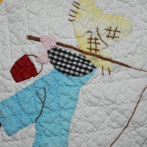 May include: A white quilted fabric square featuring an appliqued scarecrow figure with a yellow hat, black and white checkered shirt, and light blue pants. A brown stick is held over the shoulder with a red bag. A measuring tape shows 5 inches.