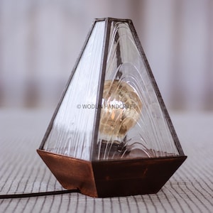 May include: A geometric glass lamp with a textured glass shade and a wooden base. The lamp is lit with a light bulb and has a cord.