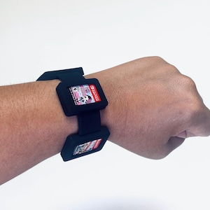 May include: Black wristband with two slots for Nintendo Switch game cartridges. The wristband is made of a soft, flexible material and has a secure closure.