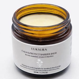May include: A jar of Luksura Calm & Protect Barrier Balm. The amber-colored glass jar contains a creamy balm. The label reads "Calm & Protect Barrier Balm" and "Protective & Comforting Balm for Sensitive & Flare-Prone Skin". The jar contains 1.7 fl oz.
