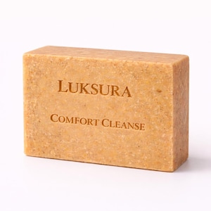 May include: A light brown rectangular soap bar, with the words "LUKSURA Comfort Cleanse" printed on it. The soap has a textured surface and is set against a white background.