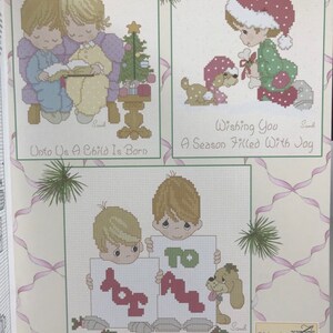 K&ouml;nnte beinhalten: Drei Kreuzstichmuster mit Precious Moments-Charakteren. Das erste Muster zeigt zwei Kinder, die auf einer Bank sitzen, mit einem Weihnachtsbaum hinter ihnen. Das zweite Muster zeigt ein Kind in einer Weihnachtsmannm&uuml;tze mit einem Hund. Das dritte Muster zeigt zwei Kinder, die Schilder halten, auf denen "Joy To All" steht.