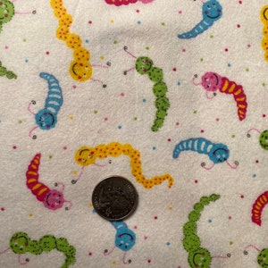Może przedstawiać: Biały materiał z powtarzającym się wzorem kolorowych, uśmiechniętych gąsienic. Gąsienice są w różnych kolorach, w tym żółtym, zielonym, niebieskim, różowym i czerwonym. Materiał ma nakrapiany wzór z małymi kolorowymi kropkami.