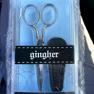 May include: A pair of silver-toned Gingher knife-edge sewing scissors measuring 4 inches in length, packaged in a clear plastic blister pack with a black sheath. The packaging features the brand name Gingher and the text Knife-edge Sewing Scissors 4 inches.