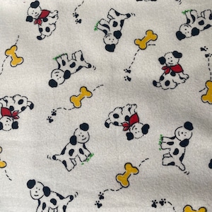 Może przedstawiać: Biały materiał z powtarzającym się wzorem czarno-białych dalmatyńczyków z czerwonymi obrożami i żółtymi kształtami kości. Materiał ma subtelną fakturę.