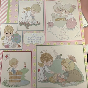 May include: A collection of four cross-stitch patterns featuring Precious Moments characters. The patterns include a boy holding a globe, two angels, a boy in a bucket, and two angels with a soldier. The title of the collection is "Precious Moments™ A Collection of Favorites Vol. 2".