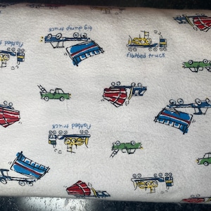 Może przedstawiać: Biały materiał z powtarzającym się wzorem kolorowych kreskówek ciężarówek. Ciężarówki są narysowane w prostym stylu i obejmują wywrotki, ciężarówki z platformą i inne rodzaje ciężarówek. Tekst "big dump truck", "flatbed truck" i "flatbed truck" jest zawarty we wzorze.