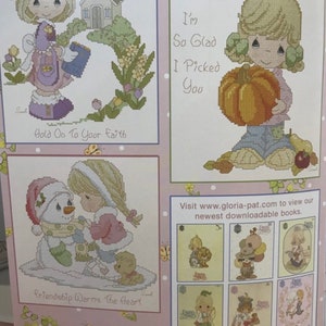 Peut inclure: Quatre motifs de point de croix mettant en scène des personnages Precious Moments. Le premier motif représente une fille tenant un arrosoir avec une petite église en arrière-plan. Le deuxième motif représente une fille tenant une citrouille. Le troisième motif représente une fille et un bonhomme de neige. Le quatrième motif représente une fille tenant un ours en peluche. Les textes "Hold On To Your Faith", "I'm So Glad I Picked You", "Friendship Warms The Heart", et "Precious Moments" sont inclus dans les motifs.