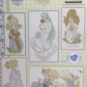 May include: A collection of four cross-stitch patterns featuring Precious Moments characters. The patterns include a girl holding a cross, a mother holding a child, a girl holding a book, and a group of children with a dog. The patterns are part of a 25th anniversary special edition.