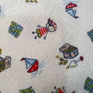 Może przedstawiać: Biała tkanina z powtarzającym się wzorem kreskówkowych piratów, skrzyń ze skarbami, map i żaglówek. Piraci noszą czerwono-białe koszule w paski, zielone szorty i czerwone bandany. Rozrzucone są złote monety.