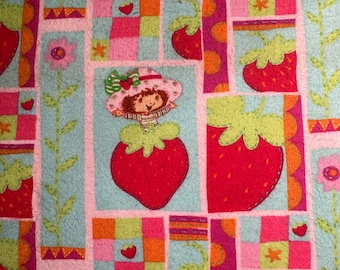 Könnte beinhalten: Ein blauer und rosa Stoff mit einem sich wiederholenden Muster aus Erdbeeren, Blumen und einer Comic-Erdbeerfigur. Der Stoff hat ein Patchwork-Design mit Quadraten in verschiedenen Farben.