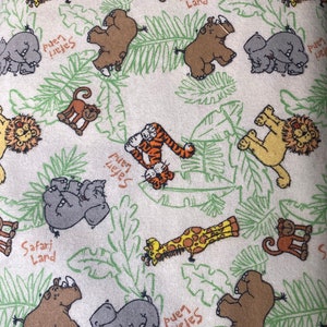 Może przedstawiać: Biała tkanina z powtarzającym się wzorem zwierząt z sawanny, w tym żyraf, słoni, nosorożców, tygrysów, małp i lwów. Tkanina zawiera również tekst "Safari Land" i "Pueri Helejes".
