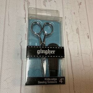 May include: Gingher 4-inch knife-edge sewing scissors in a clear plastic package. The scissors have silver blades and finger holes. The package has a black label with the brand name "gingher" in white.