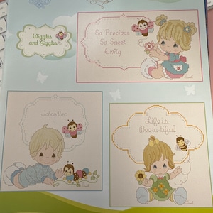 May include: A book of cross-stitch patterns featuring Precious Moments characters. The book cover shows four different designs, each with a different character and a cute saying. The designs include "Wiggles and Giggles", "So Precious So Sweet Emily", "Johnathan", and "Life is Bee-u-tiful".