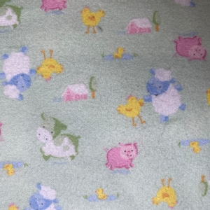 Może przedstawiać: Zielony materiał z powtarzającym się wzorem zwierząt gospodarskich, w tym świń, krów i kurcząt. Zwierzęta są wszystkie białe z różowymi, niebieskimi lub żółtymi akcentami.