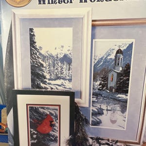 May include: A cross stitch pattern booklet titled "Winter Wonderland" featuring three framed images: a snowy mountain scene, a church in a snowy landscape, and a red cardinal in a snowy setting. The booklet includes the text "Counted Cross Stitch designs by Sherrie Stepp-Aweau."